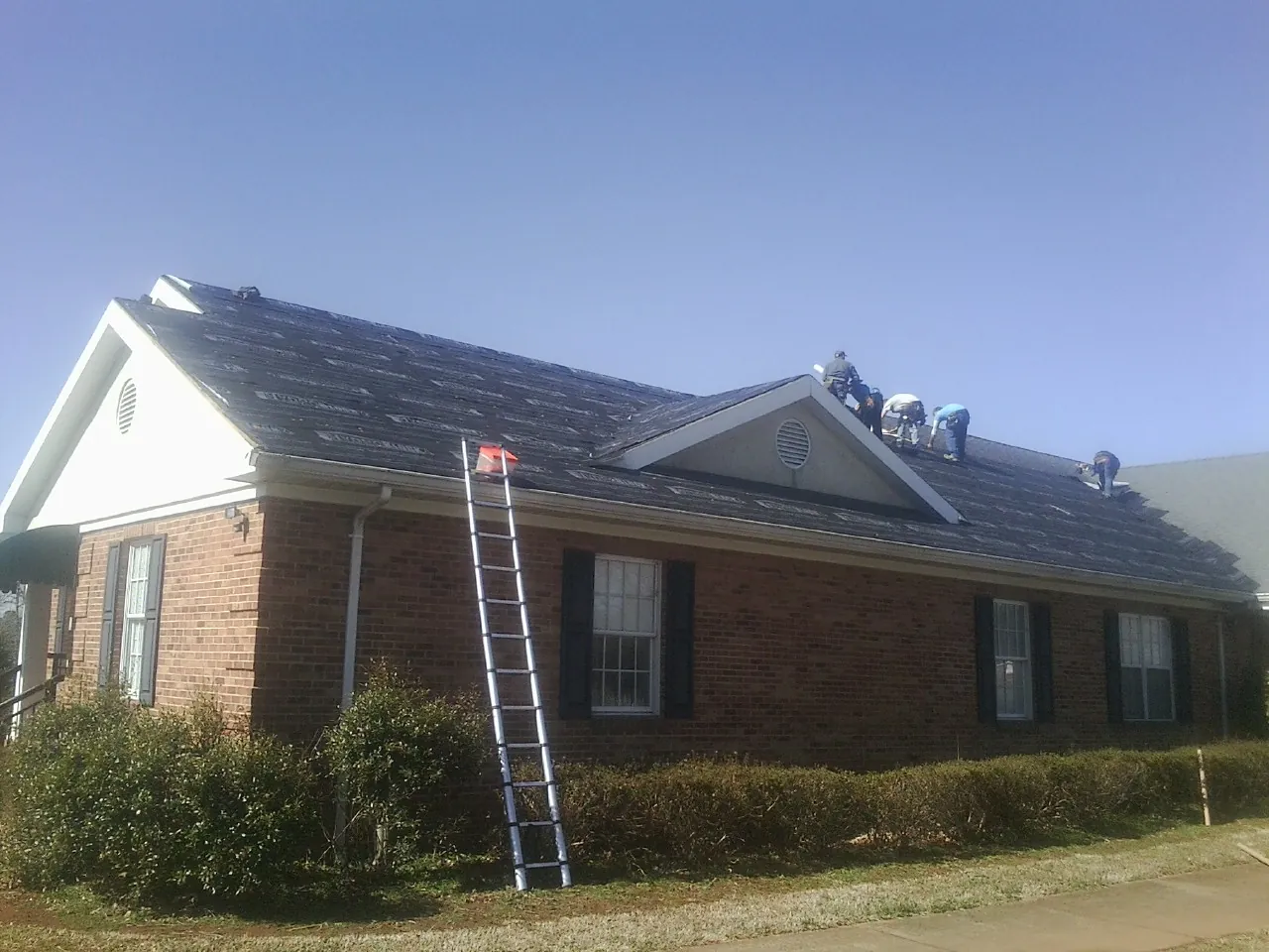 Crew tearing shingles off a brick ranch roof with a ladder set — Metal Roof Repair work by our crew in Raywood