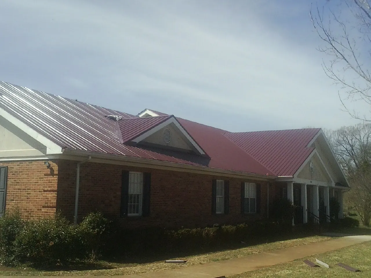 Red metal roof with gabled entries on a long brick building, from a Hail Damage Roof Repair job in Raywood