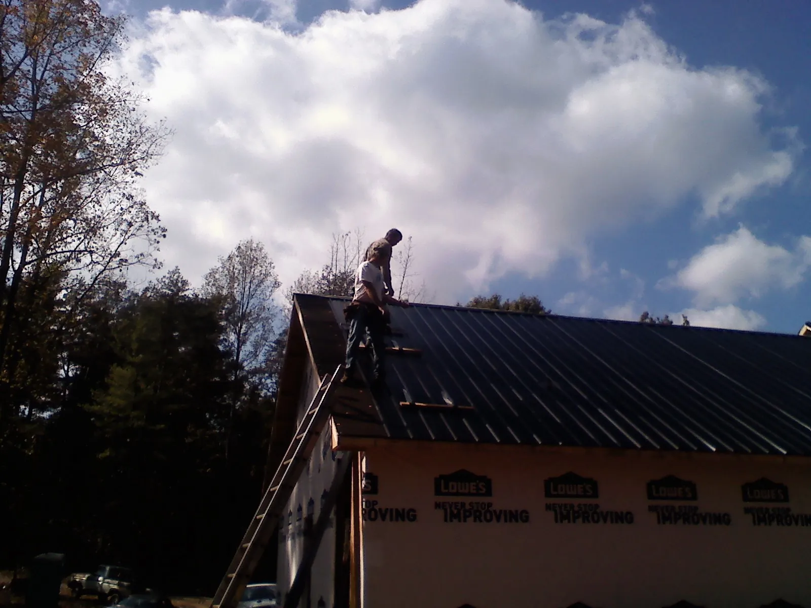 Roofer fastening dark metal panels high against a cloudy sky, from a Roof Inspection job in Raywood