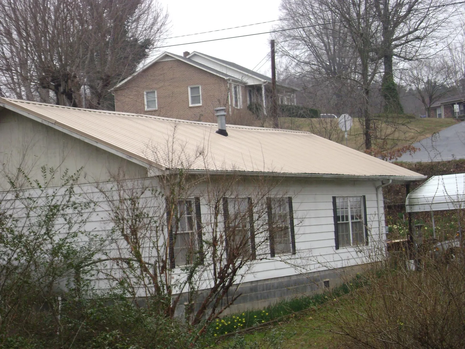 Tan metal roof on a white sided house set into a hillside — Commercial Roofing by Roofing Brothers in Raywood